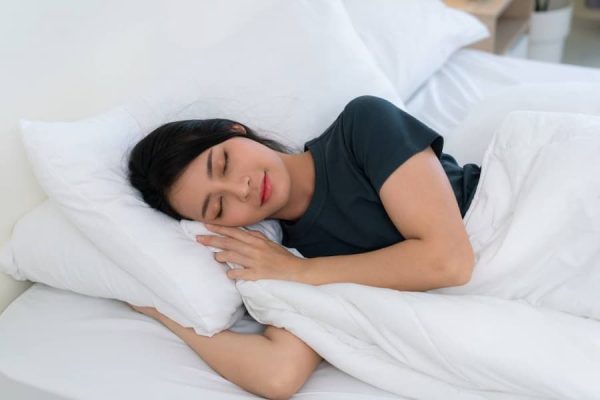 A woman comfortably asleep under white sheets, illustrating the connection between sleep quality and sensitive skin concerns.